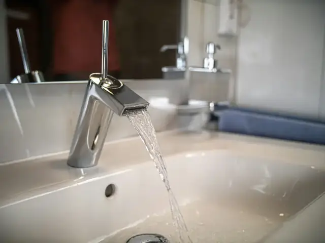 Chrome faucet with water flowing into a white basin