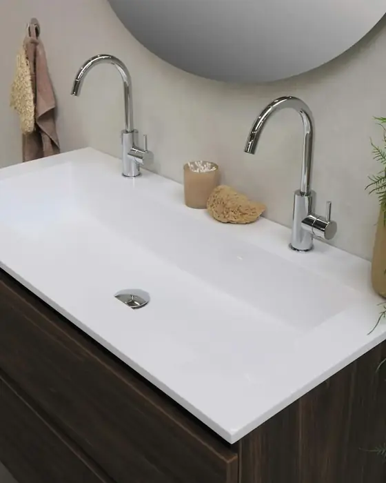 Modern basin with two chrome faucets on a dark wooden vanity