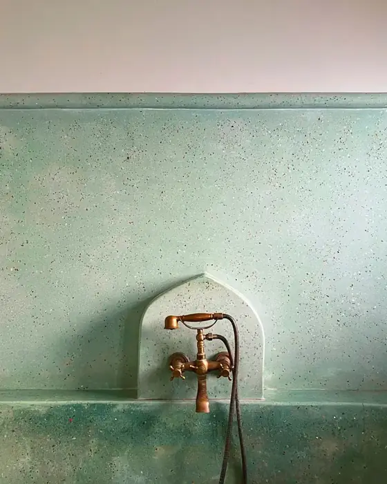 Brass wall-mounted bath mixer over a green tiled tub